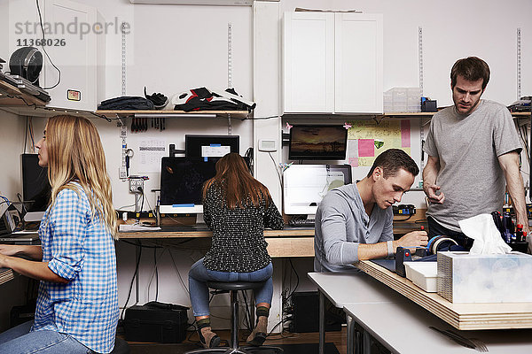 Zwei Frauen und zwei Männer in einer technischen Reparaturwerkstatt oder einem Labor  die an Computern arbeiten.