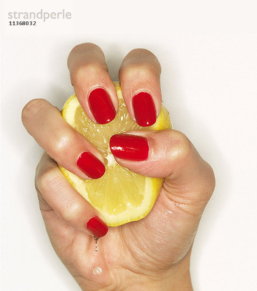 Hand einer Frau mit rotem Nagellack  die eine Zitrone auspresst