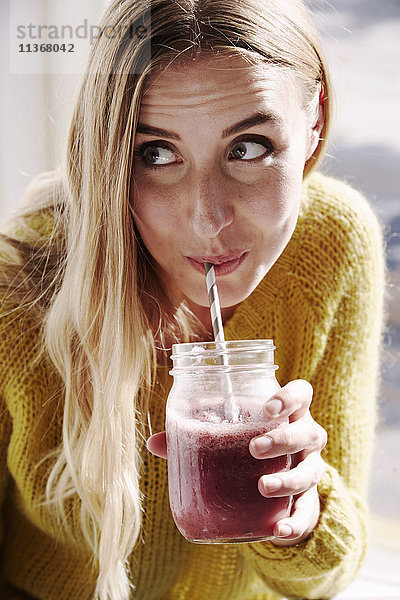 Eine junge Frau beugt sich vor und schlürft einen Smoothie aus einem Strohhalm.