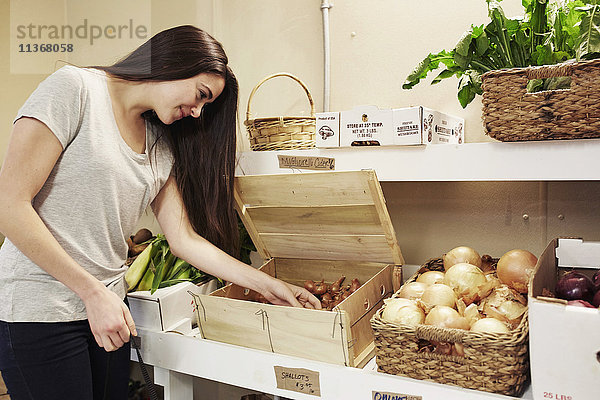 Eine Frau wählt Gemüse aus einer Auslage in einem Hofladen aus.