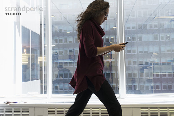 Junge Frau mit Mobiltelefon vor einem Fenster