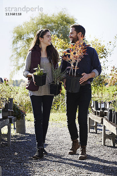 Ein junger Mann und eine junge Frau gehen durch die Auslagen eines Gartenzentrums  halten Pflanzen und schauen sich gegenseitig an.