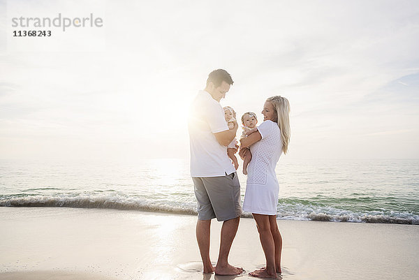 Glückliche Familie mit zwei kleinen Mädchen (2-5 Monate) am Strand im Sonnenlicht