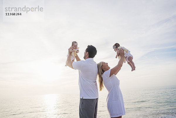 Glückliche Familie mit zwei kleinen Mädchen (2-5 Monate) am Strand im Sonnenlicht