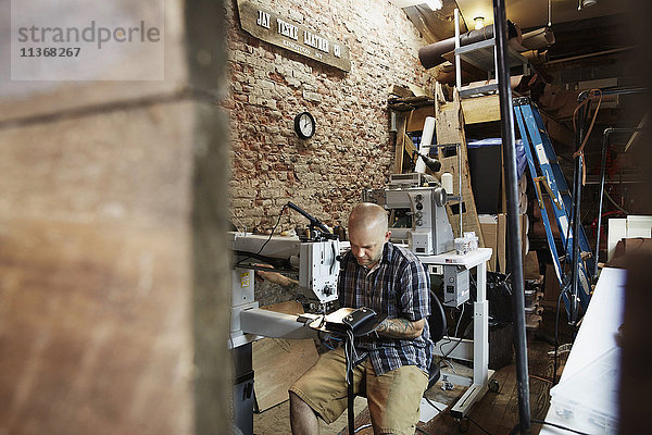 Ein Lederarbeiter  Handwerker  der eine Industrienähmaschine auf Ledermaterial in seiner Werkstatt benutzt.