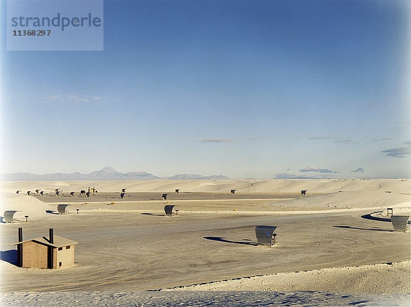 Ein offener Raum  eine Wüstenlandschaft  mit einer kleinen Hütte und Sonnenunterständen  umgeben von Bergen.