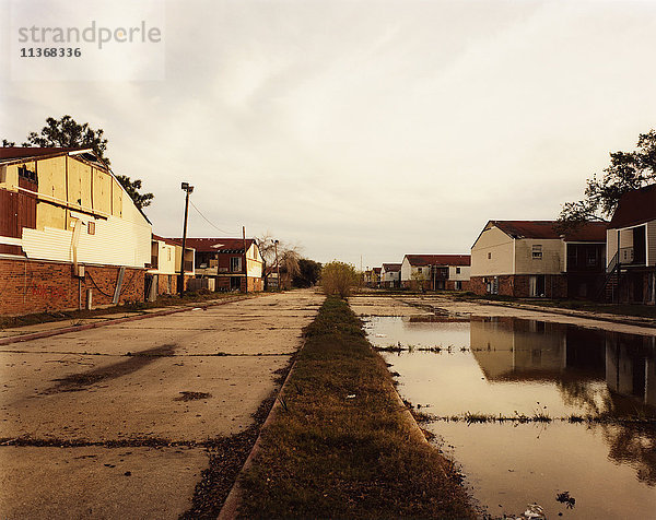 Eine menschenleere Straße mit rissigen Pflasterungen und Pfützen und Industriegebäuden.