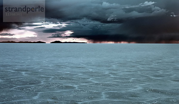 Salzebenen  ein rissiges Muster in der Bodenkruste  Blick zum Horizont und schwarze Gewitterwolken und Lichtflecken am Himmel.