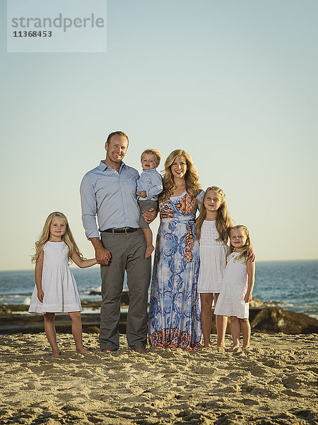 Familie mit Kindern (12-17 Monate  4-5  6-7  8-9) am Strand stehend mit Meer im Hintergrund