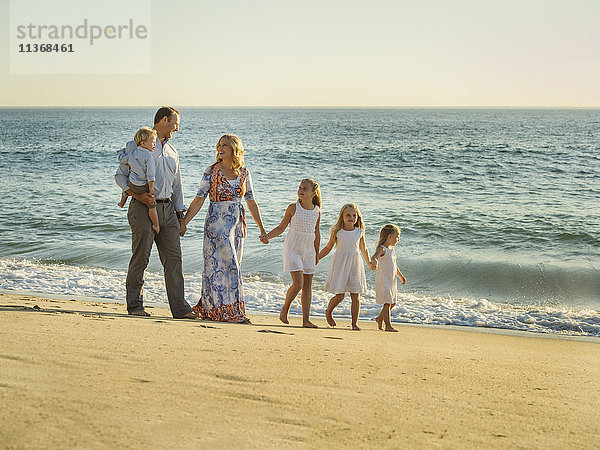 Familie mit Kindern (12-17 Monate  4-5  6-7  8-9) beim Spaziergang am Strand mit Meer im Hintergrund