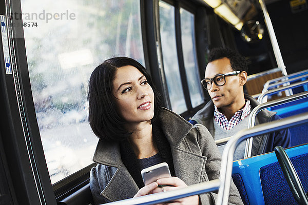 Ein junger Mann und eine junge Frau sitzen in öffentlichen Verkehrsmitteln  halten ihre Mobiltelefone in der Hand und schauen sich um.