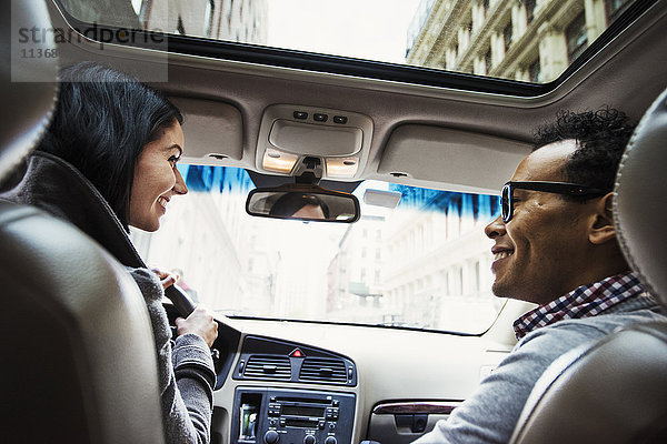 Eine junge Frau und ein junger Mann in einem Auto  die sich vom Rücksitz aus gesehen lächelnd ansehen.