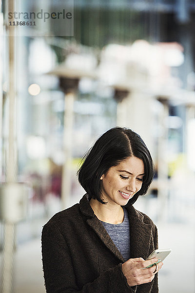 Eine junge Frau hält ein Handy in der Hand und lächelt.