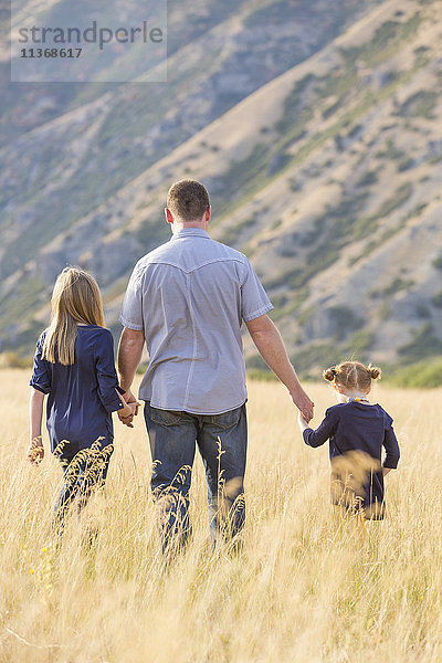 Vater mit zwei Töchtern (4-5  8-9) beim Spaziergang auf einem Feld