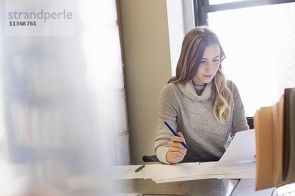 Eine junge Frau sitzt an einem Schreibtisch in einem Büro und sieht sich Papierkram an.