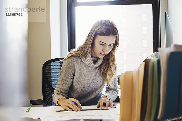 Eine junge Frau sitzt an einem Schreibtisch in einem Büro und tippt.