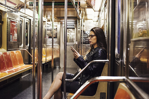 Eine Frau sitzt in einem U-Bahnwagen und schaut auf ihr Handy.