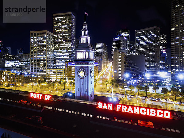 Blick aus der Luft auf das Fährgebäude in San Francisco  bei Nacht. Die städtischen Gebäude der Innenstadt und die Gebäude am Wasser.
