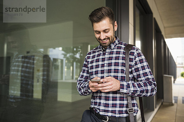 Junger Mann schreibt eine SMS auf seinem Handy und lächelt