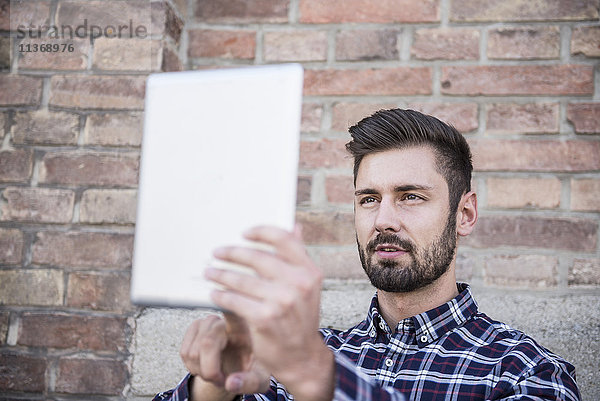 Junger Mann nimmt Selfie mit digitalen Tablette gegen Backsteinmauer