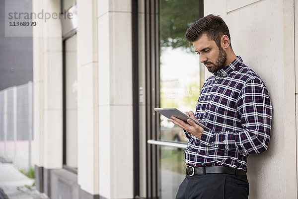 Junger Mann arbeitet an einem digitalen Tablet an der Wand