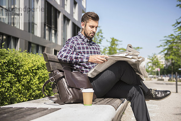 Junger Mann sitzt auf einer Bank und liest Zeitung