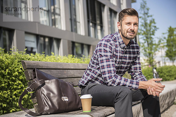 Junger Mann sitzt mit Kaffee auf einer Bank