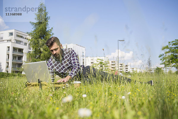 Junger Mann arbeitet am Laptop und liegt im Park