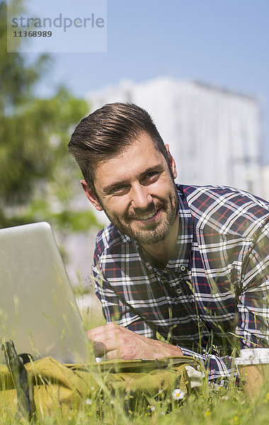 Junger Mann arbeitet am Laptop und liegt im Park