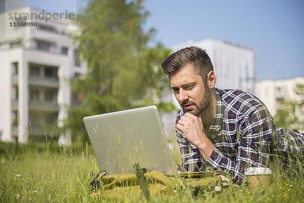 Junger Mann arbeitet am Laptop und liegt im Park