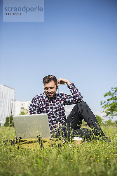 Junger Mann arbeitet am Laptop und sitzt im Park