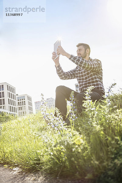 Junger Mann nimmt Selbstporträtfotografie mit digitalem Tablet im Park