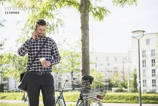 Junger Mann telefoniert mit dem Handy und trinkt Kaffee