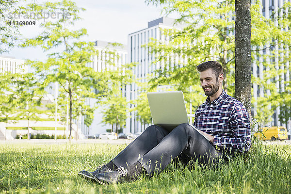 Junger Mann arbeitet am Laptop und sitzt im Park