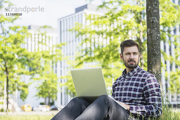 Junger Mann arbeitet am Laptop und sitzt im Park