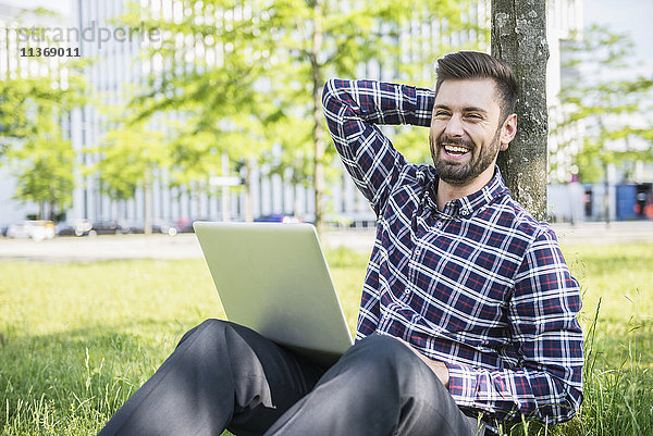 Junger Mann arbeitet am Laptop und sitzt im Park