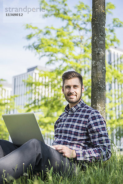 Junger Mann arbeitet am Laptop und sitzt im Park