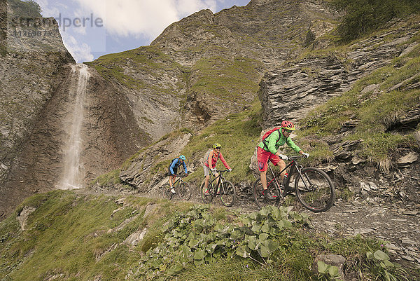 Drei Mountainbiker fahren auf einem Hügel bei einem Wasserfall  Zillertal  Tirol  Österreich