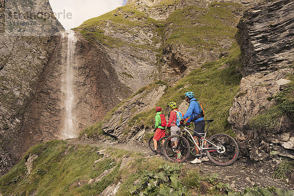 Drei befreundete Mountainbiker beobachten einen Wasserfall  Zillertal  Tirol  Österreich