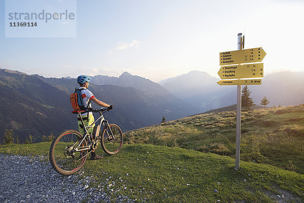 Rückansicht eines Mountainbikers  der in der alpinen Landschaft steht und die Aussicht bei Sonnenuntergang betrachtet  Zillertal  Tirol  Österreich