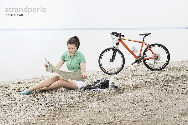 Reife Frau mit Elektrofahrrad am See mit Blick auf die Straßenkarte