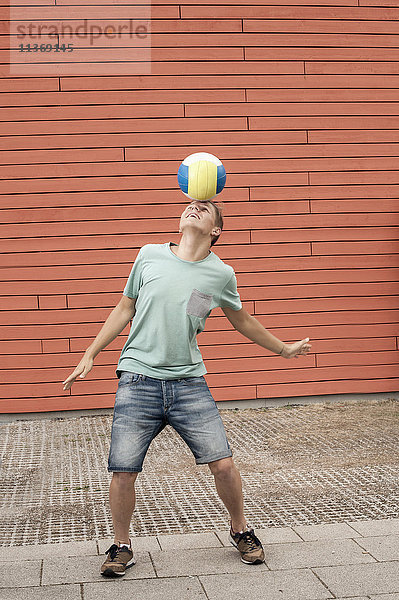 Junger Mann balanciert Ball auf der Stirn