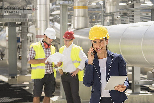 Eine Ingenieurin telefoniert mit ihrem Kollegen  der im Hintergrund diskutiert