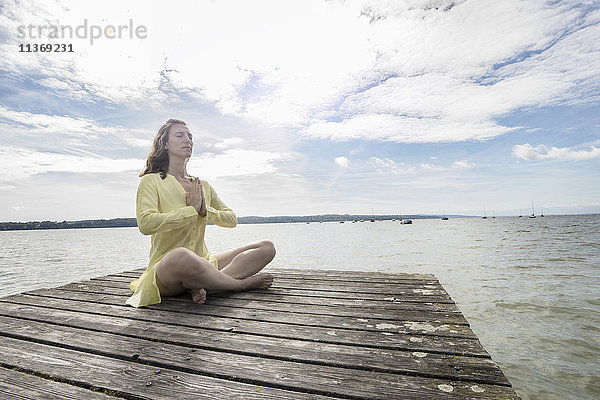 Frau beim Yoga im Lotussitz auf dem Steg am See  Ammersee  Oberbayern  Deutschland