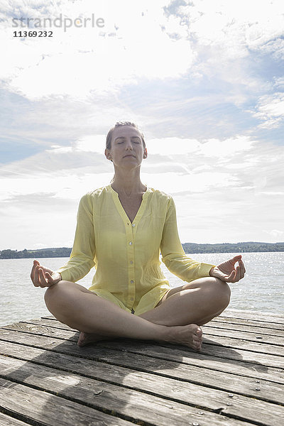 Frau beim Yoga im Lotussitz auf dem Steg am See  Ammersee  Oberbayern  Deutschland