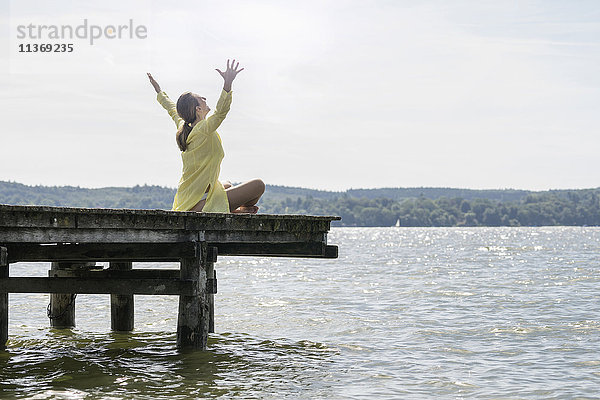 Frau mit erhobenen Armen auf der Uferpromenade am See sitzend  Ammersee  Oberbayern  Deutschland