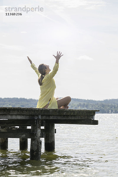 Frau mit erhobenen Armen auf der Uferpromenade am See sitzend  Ammersee  Oberbayern  Deutschland