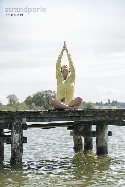 Frau beim Yoga im Lotussitz auf dem Steg am See  Ammersee  Oberbayern  Deutschland