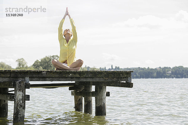 Frau beim Yoga im Lotussitz auf dem Steg am See  Ammersee  Oberbayern  Deutschland