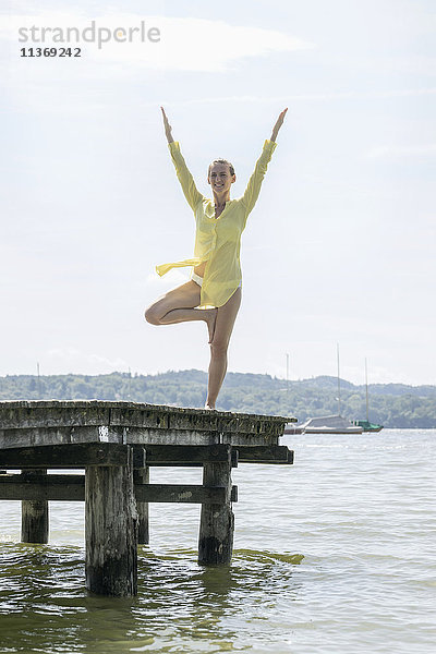 Frau macht Yoga mit erhobenen Armen und steht auf einem Steg am See  Ammersee  Oberbayern  Deutschland